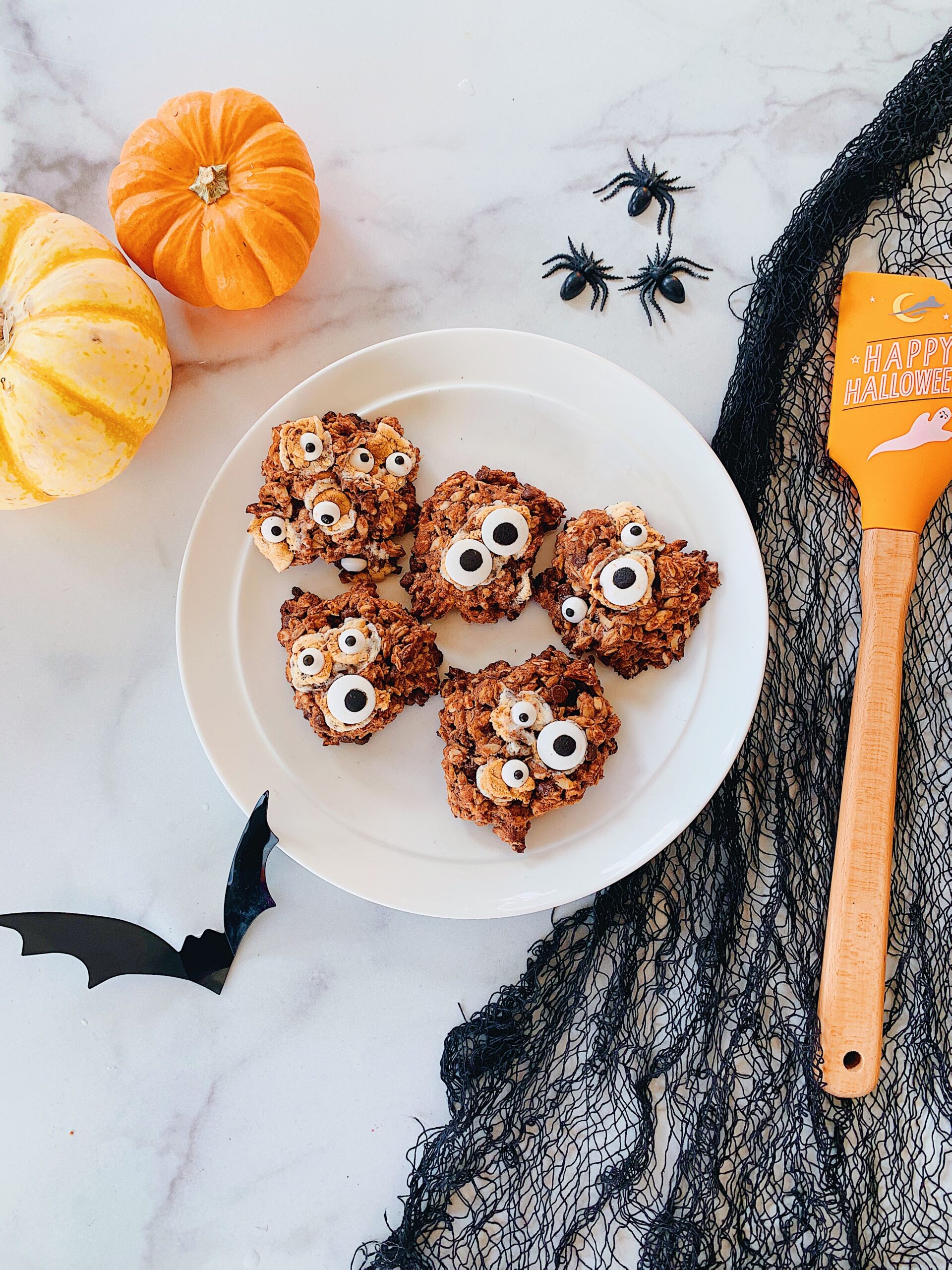 A plate of Halloween themed monster cookies with googly eyes in spooky setting.