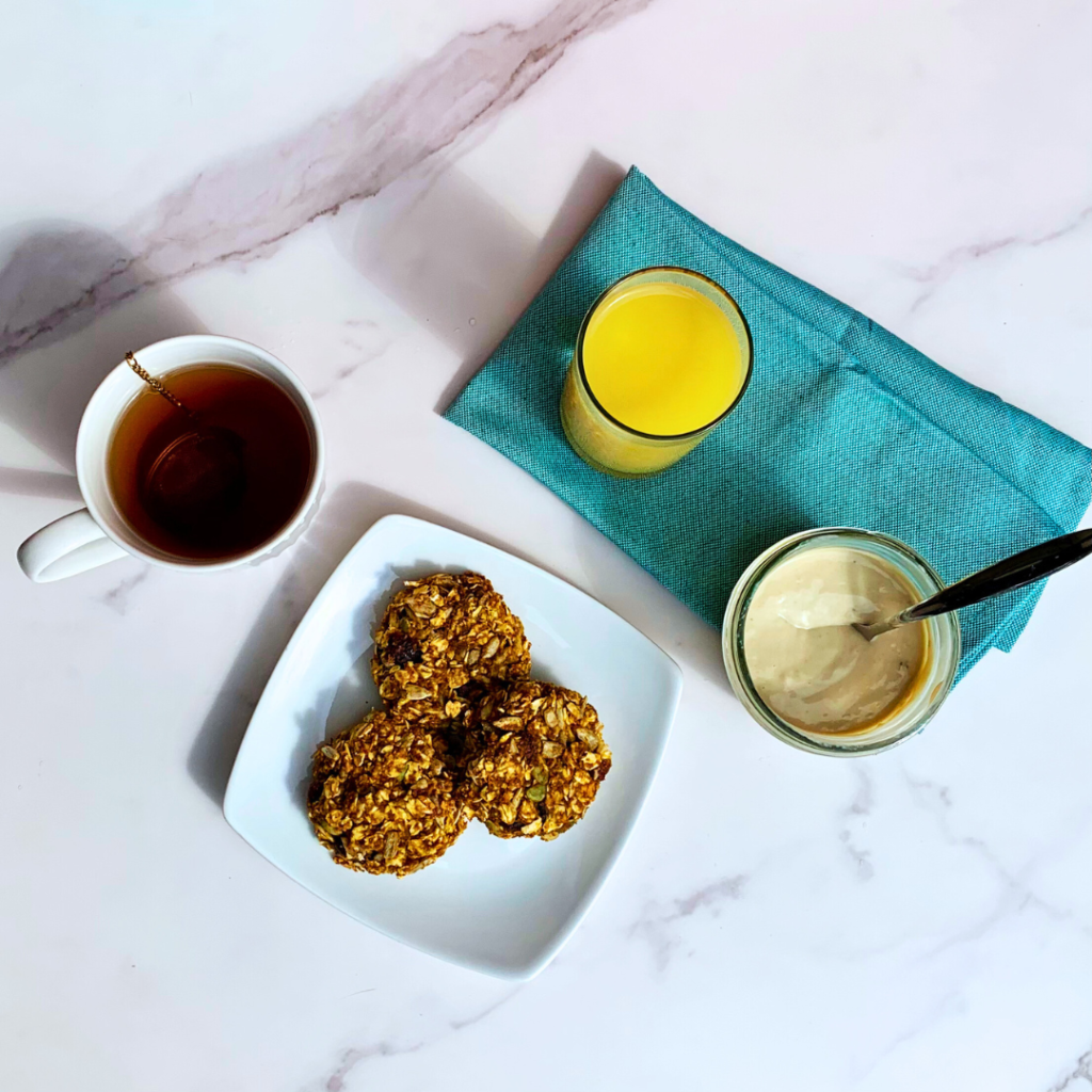 ZEGO organic muesli gluten-Free breakfast cookies with vanilla yogurt, a cup of hot tea, and a glass of orange juice on a blue linen napkin. 